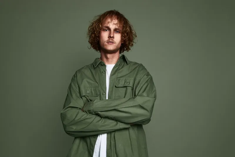 Artiest met krullen en groen overshirt tegen een groene achtergrond